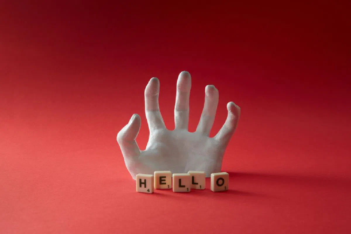 A surreal image of a hand emerging from a red background with Scrabble tiles spelling 'Hello'.