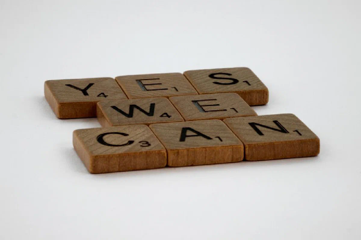 Scrabble tiles spelling 'Yes We Can' on a white background, conveying encouragement.