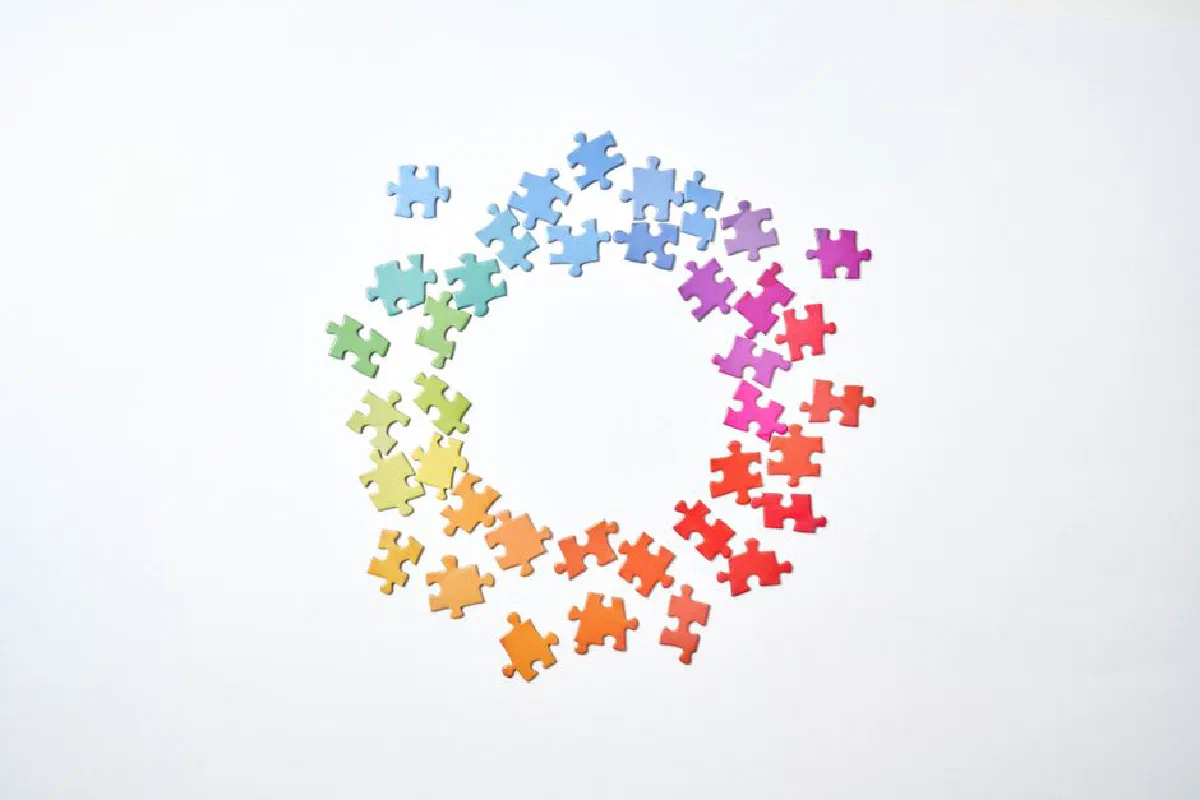 A circle formed by rainbow-colored puzzle pieces on a white background symbolizing unity and diversity.