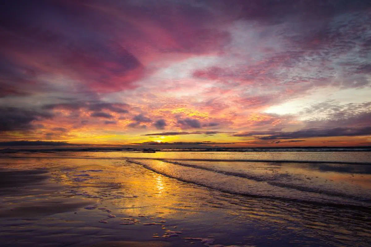 Vibrant sunset over serene ocean with dramatic clouds reflecting on the water.