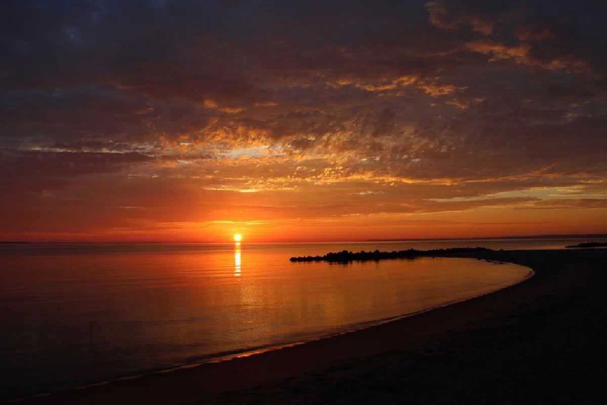 Dramatic sunset over a tranquil beach with vibrant reflections on calm water.