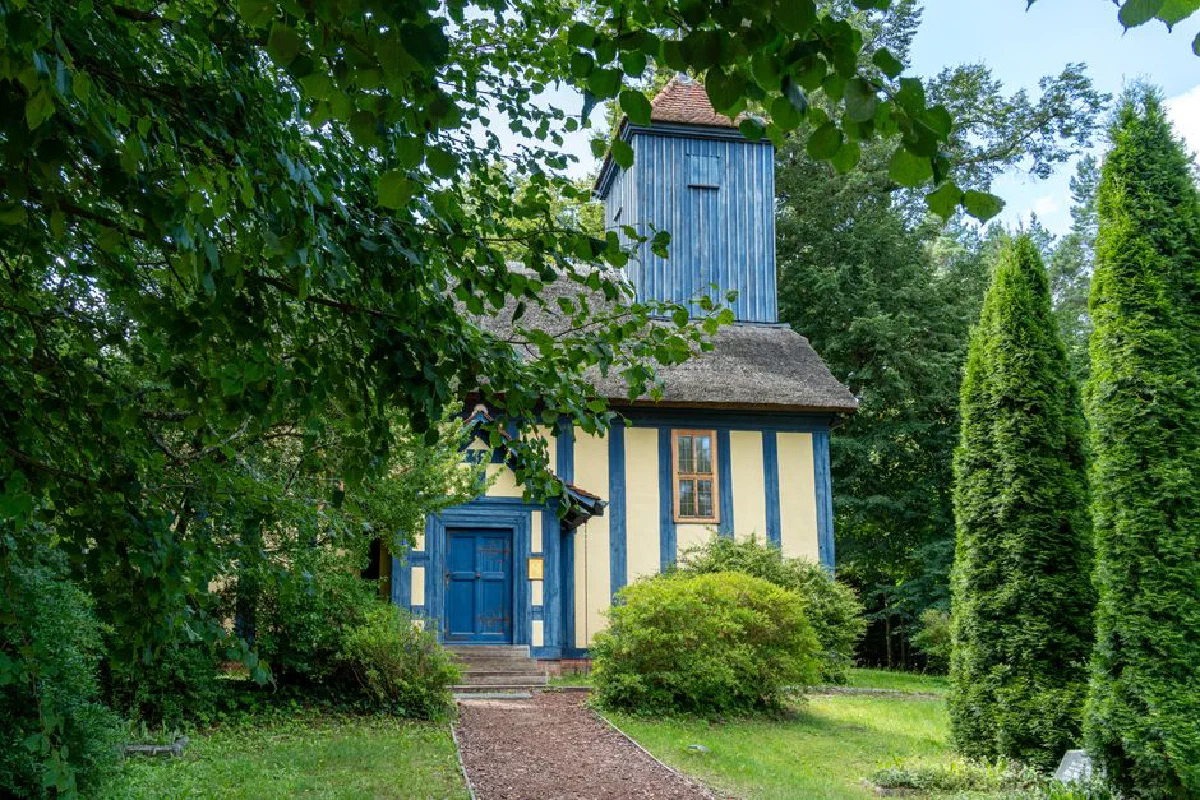 Explore a picturesque wooden church nestled in vibrant greenery under a clear summer sky.