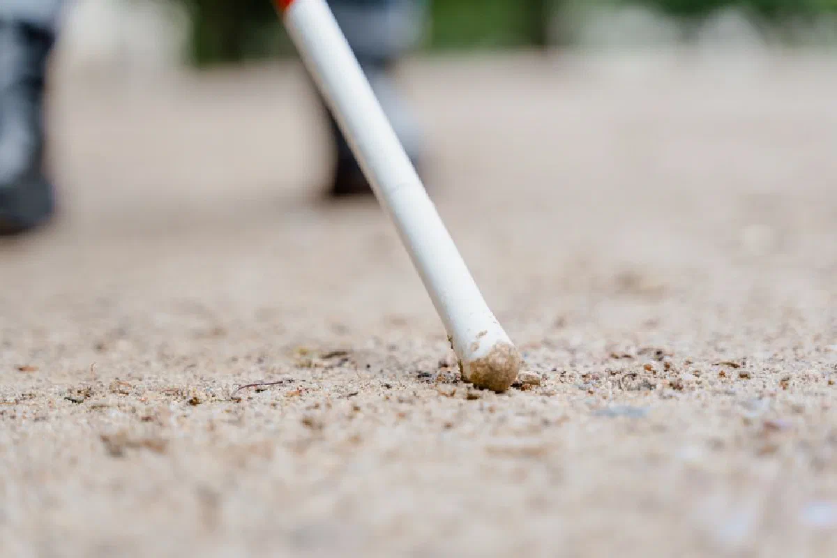 Detailed shot of a white cane on a sandy path symbolizing mobility for the visually impaired.