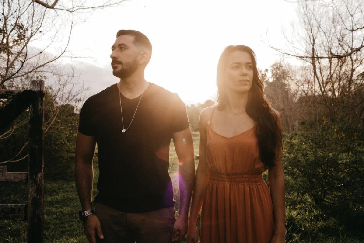 Young dreamy Hispanic man standing close to charming girlfriend while looking away on pathway in sunshine