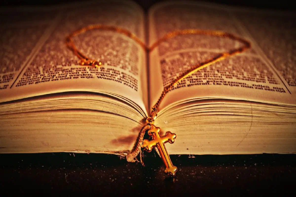 A detailed close-up of an open Bible with a golden cross necklace lying on its pages, creating a spiritual and reflective mood.