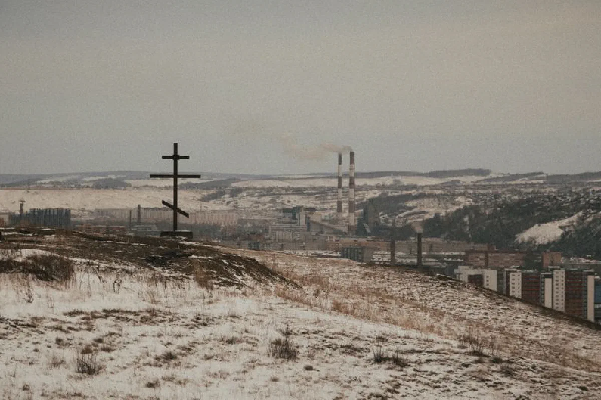 A snowy landscape featuring an industrial town and a cross, capturing winter's chill.
