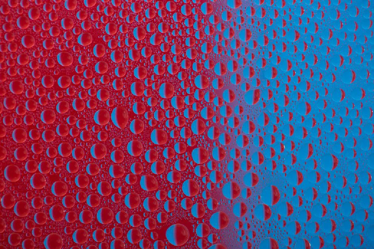 Close-up of water droplets on a vibrant red and blue surface showcasing abstract patterns.
