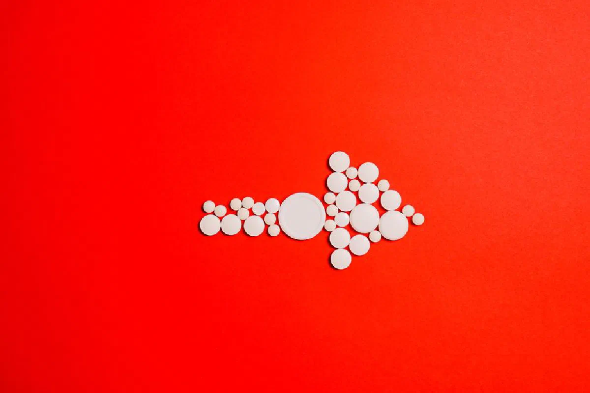 White pills form an arrow shape on a bold red backdrop, symbolizing direction in healthcare.
