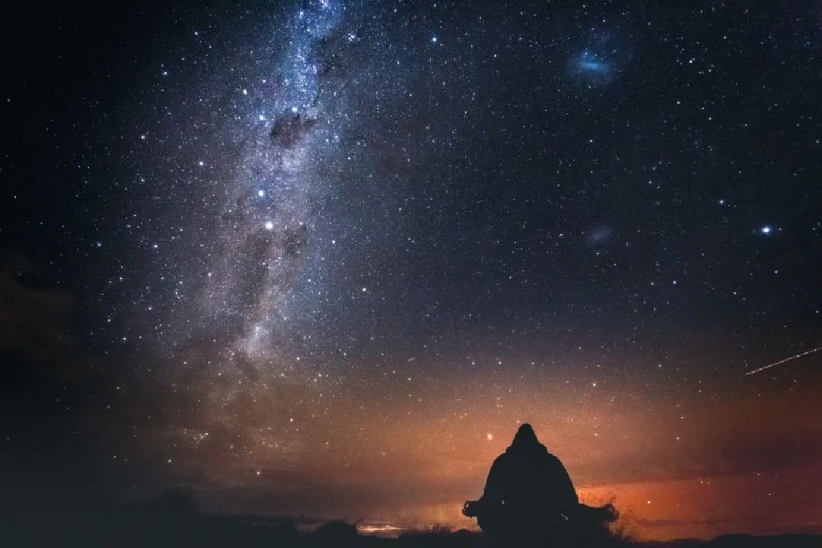 A lone figure sits under a starry sky with the Milky Way visible, capturing the beauty of a New Zealand night.