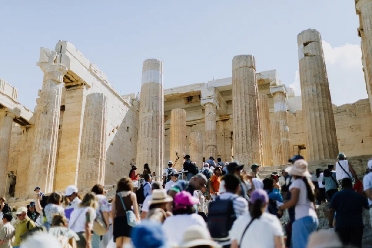 Crowds of tourists visiting the ancient Parthenon in Athens, Greece, under a clear blue sky.