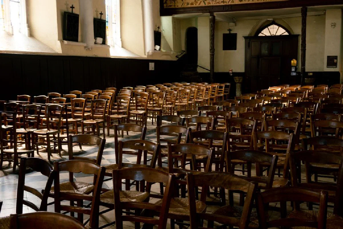 A serene church interior in France featuring rows of wooden chairs illuminated by warm sunlight through the windows.