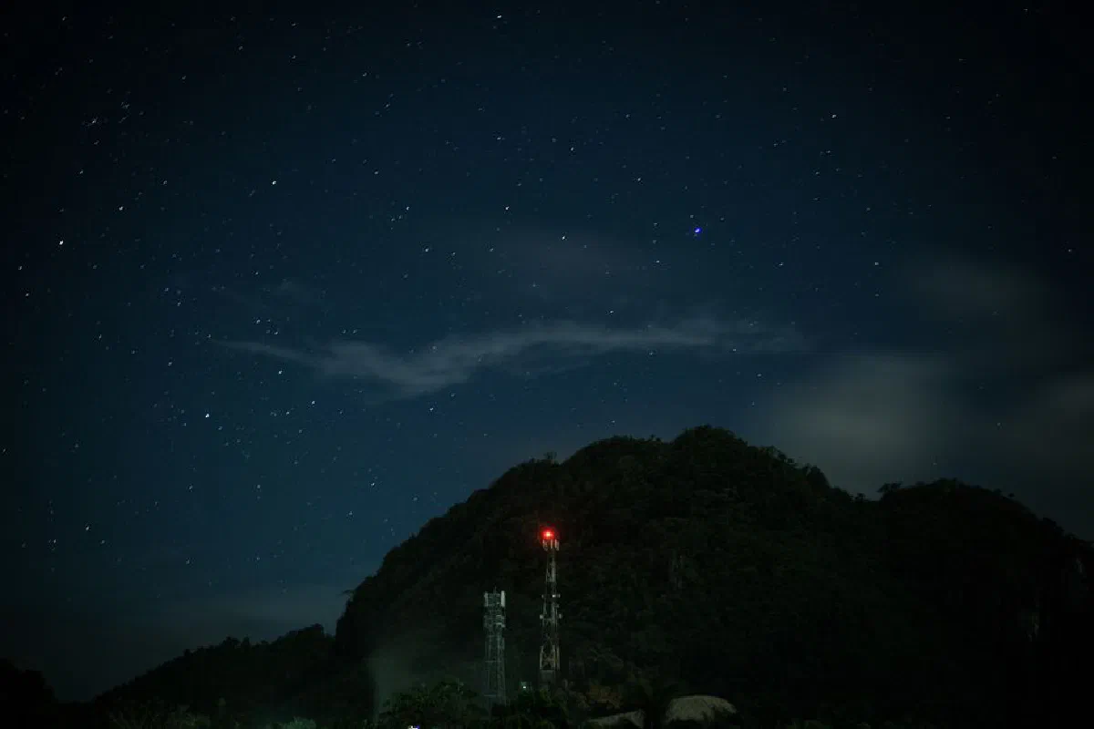 A mesmerizing starry night sky with a mountain silhouette and a glowing tower.