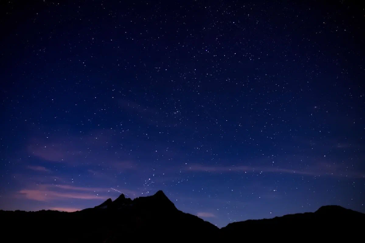 Silhouette of majestic mountain range located against dark sky with glowing bright stars in nature at night time in highland