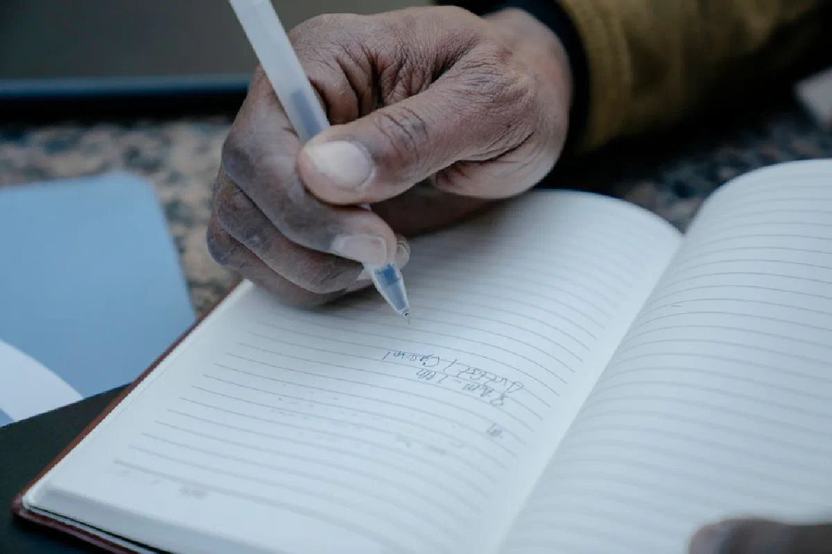 A close-up of a hand writing notes in a lined notebook with a pen.