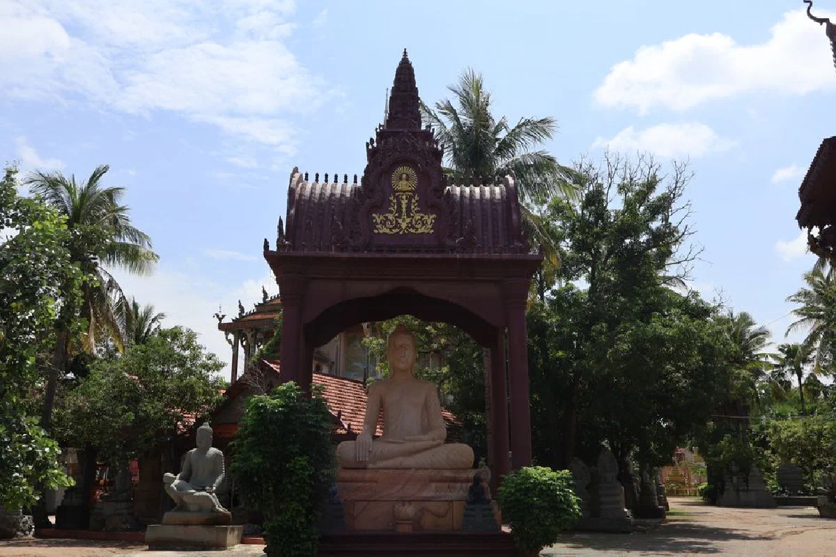 Serene temple with Buddha statue under ornate pavilion surrounded by lush trees.