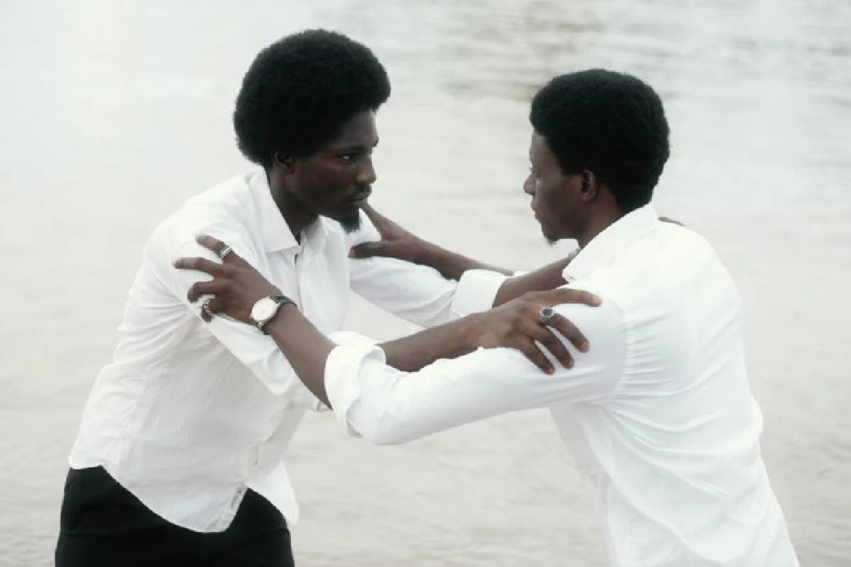 Two men in white shirts sharing an embrace by a calm water surface.