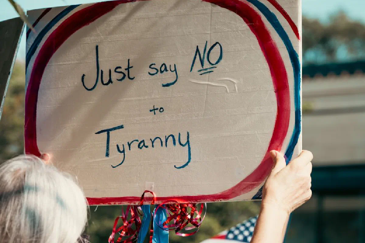Protester holding a sign reading 'Just say NO to Tyranny'. Advocacy scene outdoors.