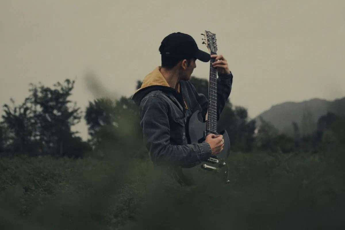 A man plays an electric guitar in a serene countryside setting, embracing the rural calm.