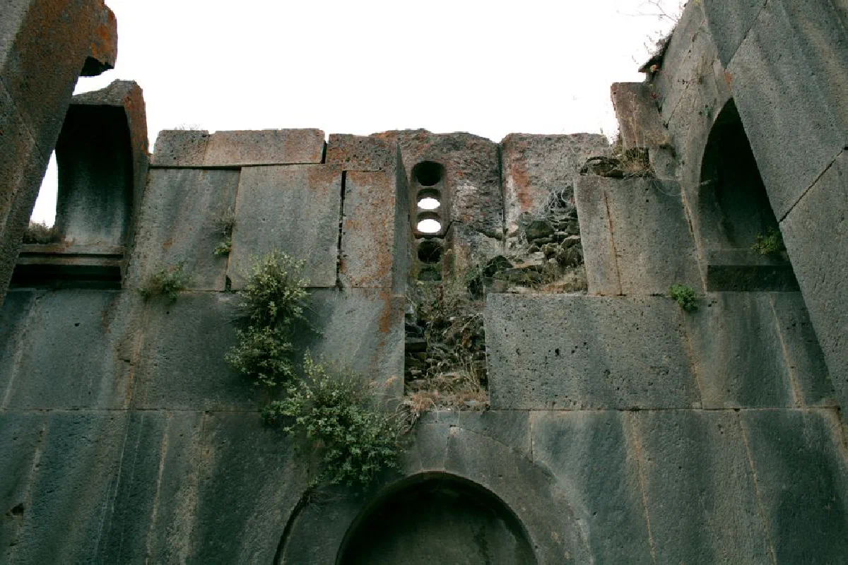 Weathered stone wall with openings, showcasing ancient architectural design.