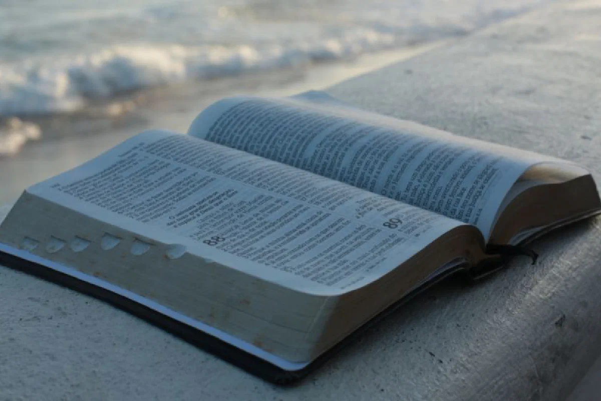 An open Bible on a concrete surface by the beach, evoking peace and reflection.