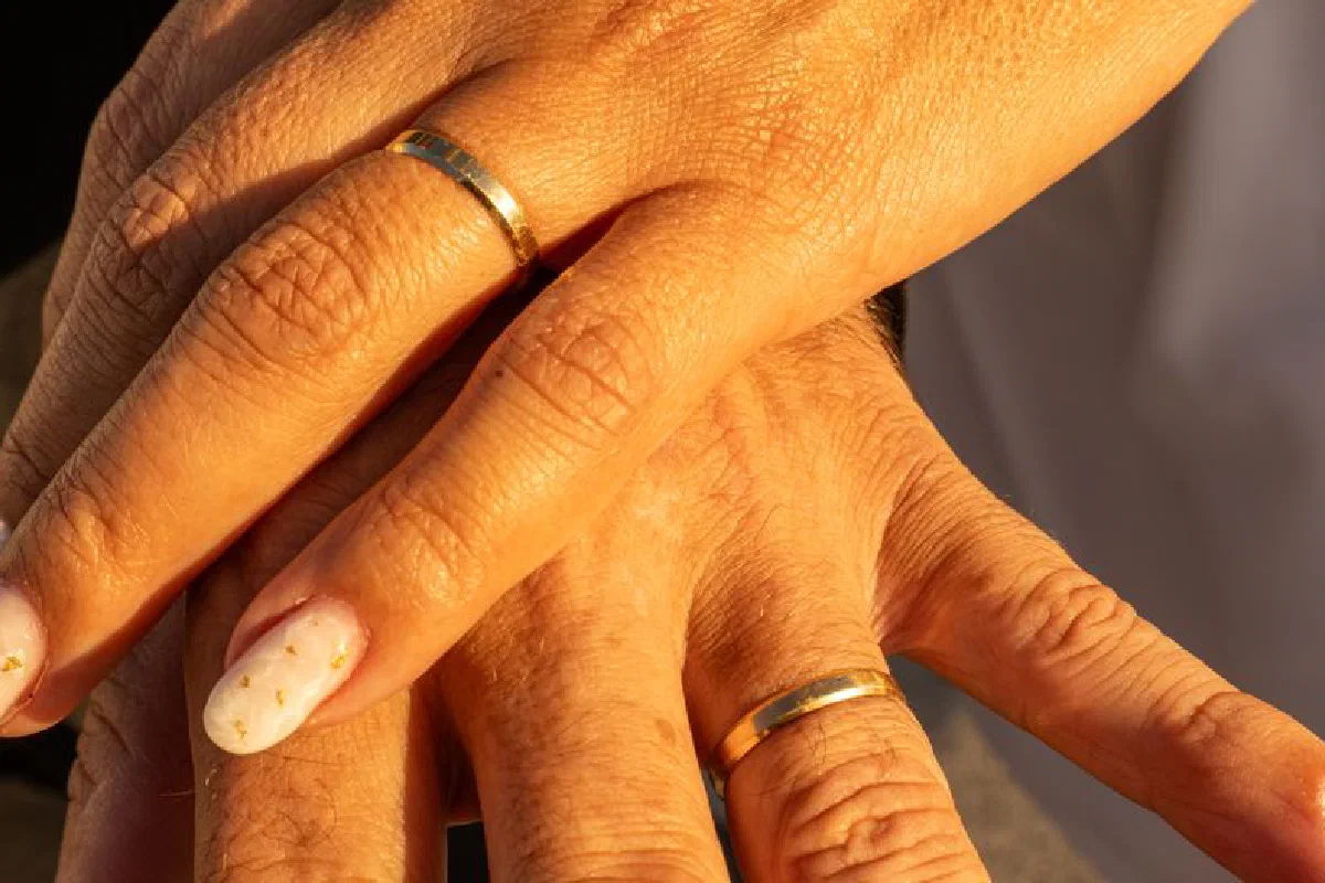 Close-up of intertwined hands wearing golden wedding rings, symbolizing love and commitment.