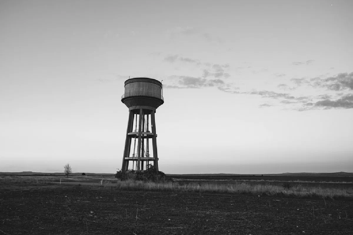Monochrome image of a solitary water tower standing in a vast, open field under a serene sky.