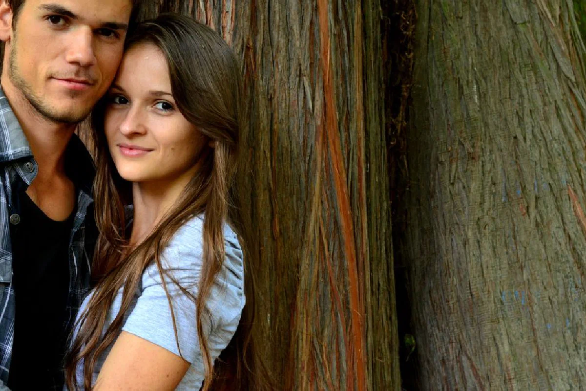 Young couple embracing outdoors against a rustic wooden background, conveying love and connection.