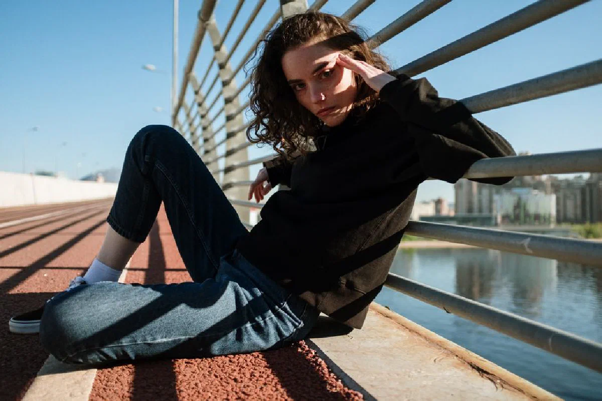A stylish young woman poses on an urban boardwalk, casting intriguing shadows.