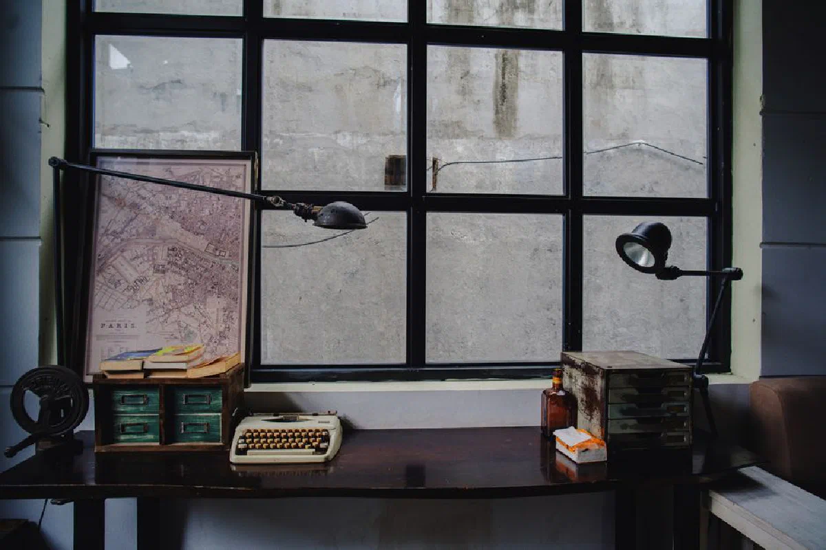 A vintage office desk setup featuring a typewriter, Paris map, and classic decor by a window.