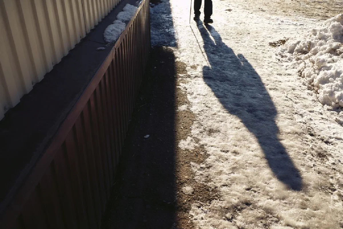 Silhouette of a person walking along a sunlit icy path, creating long shadows.