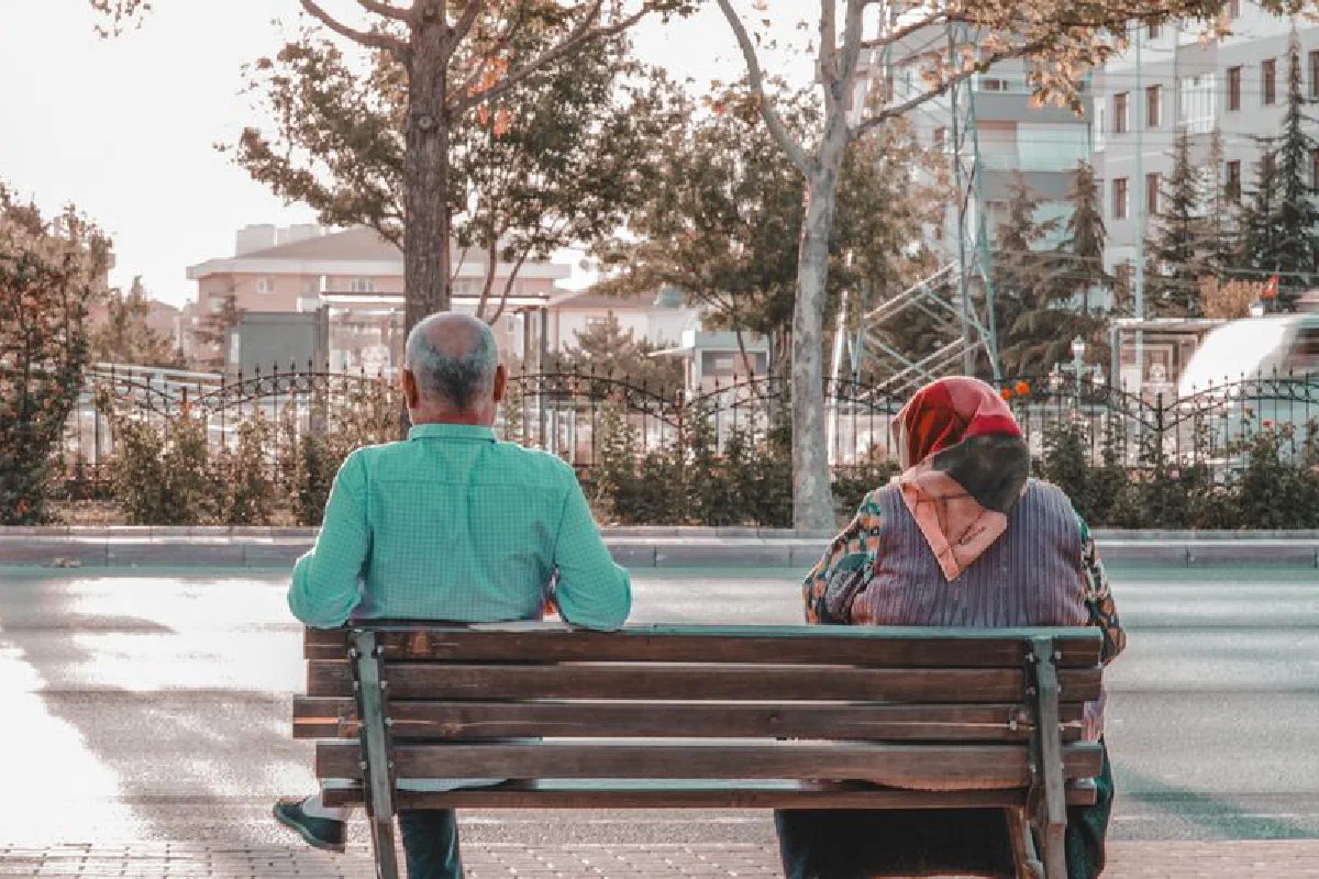 An elderly couple sits together on a bench in Konya, observing the city life around them.
