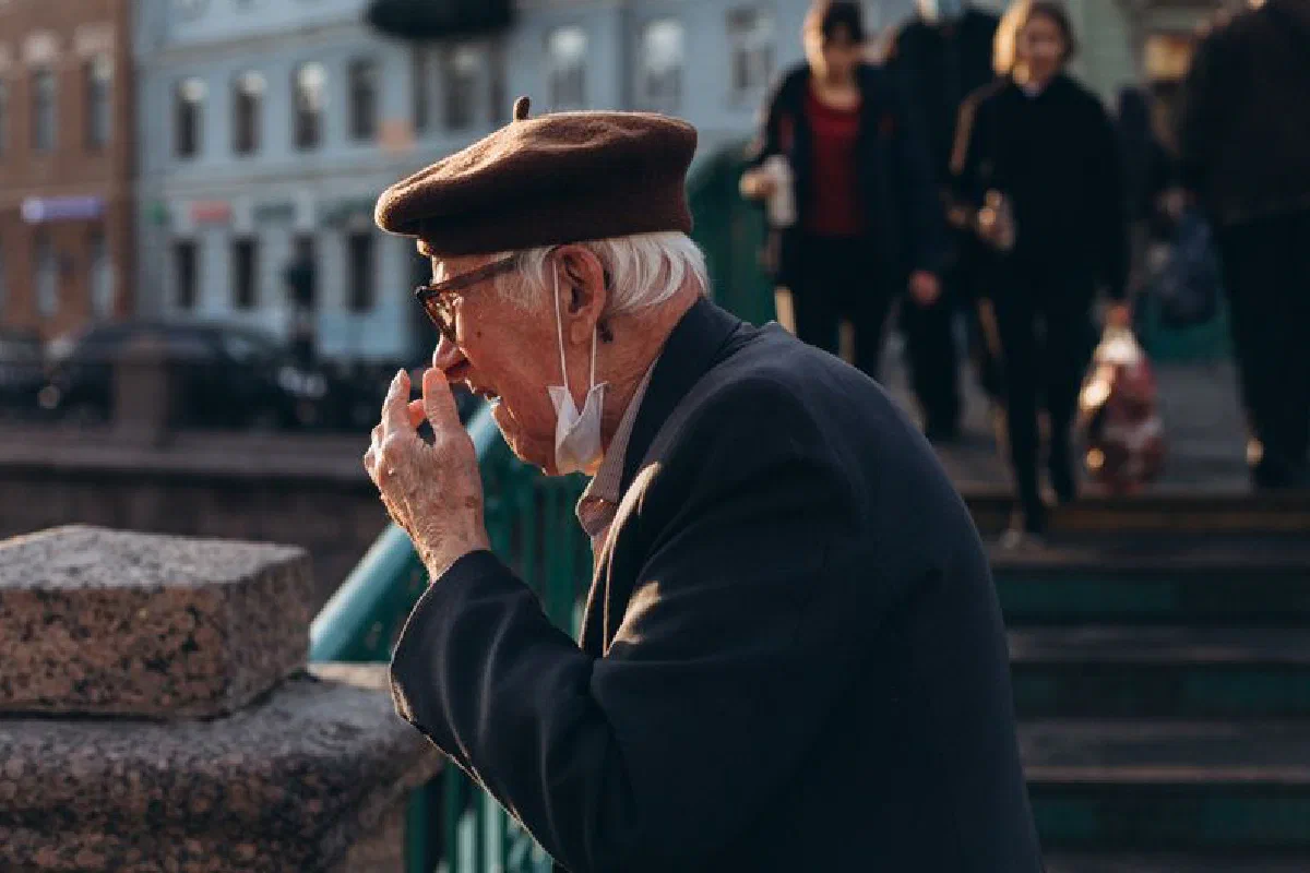 Senior man wearing a beret and facemask outdoors, side view in urban setting.