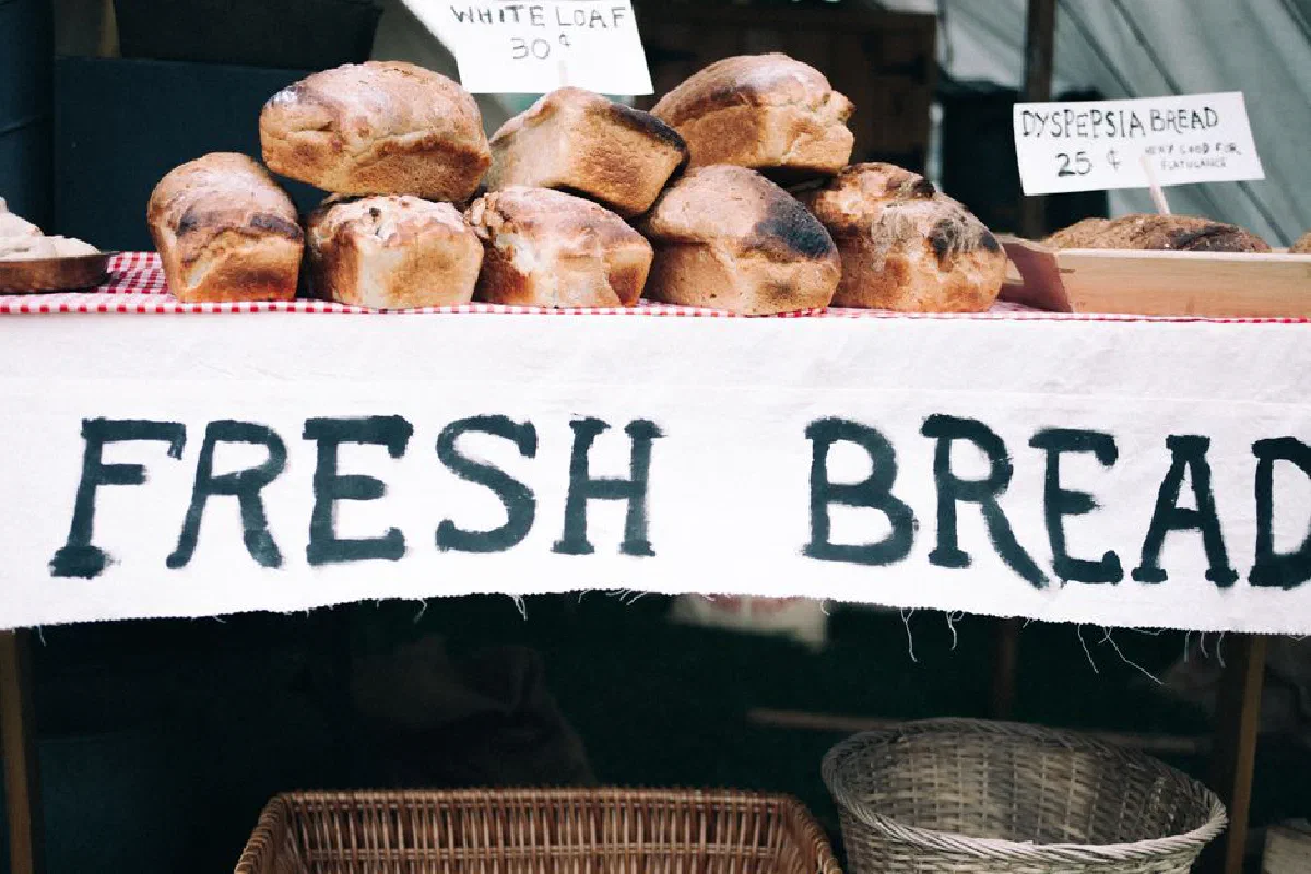 Loaves of fresh bread on display at a market stall with hand-painted signs.
