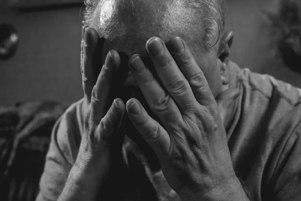 Elderly man covering face with hands, evoking emotions of sadness and stress.
