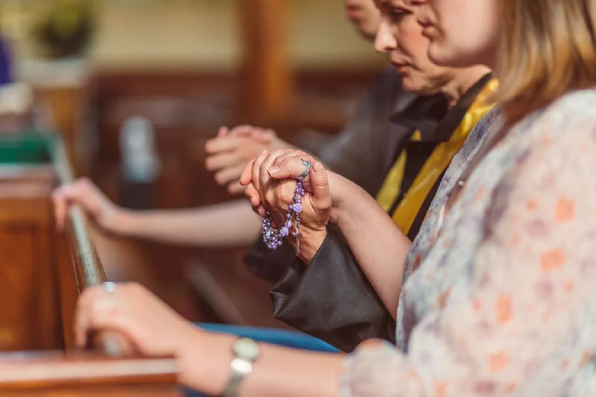 Group of people praying with rosary beads in a church, conveying faith and spirituality.