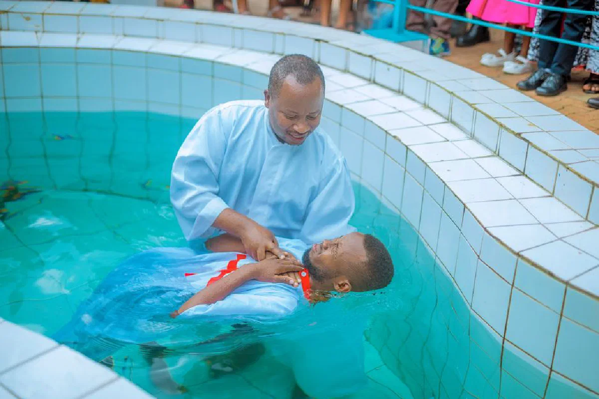 A religious baptism ceremony in an outdoor pool with a pastor immersing a man.