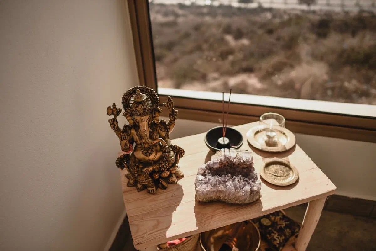A Ganesha statue with incense sticks and an amethyst crystal on a wooden table by a window.