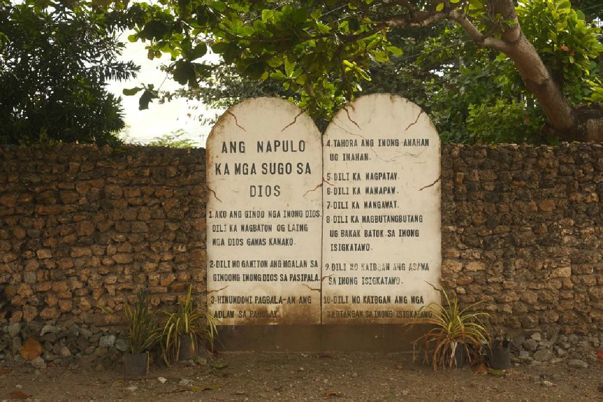 Stone tablet inscribed with religious text, set against a rustic wall in Central Visayas, Philippines.