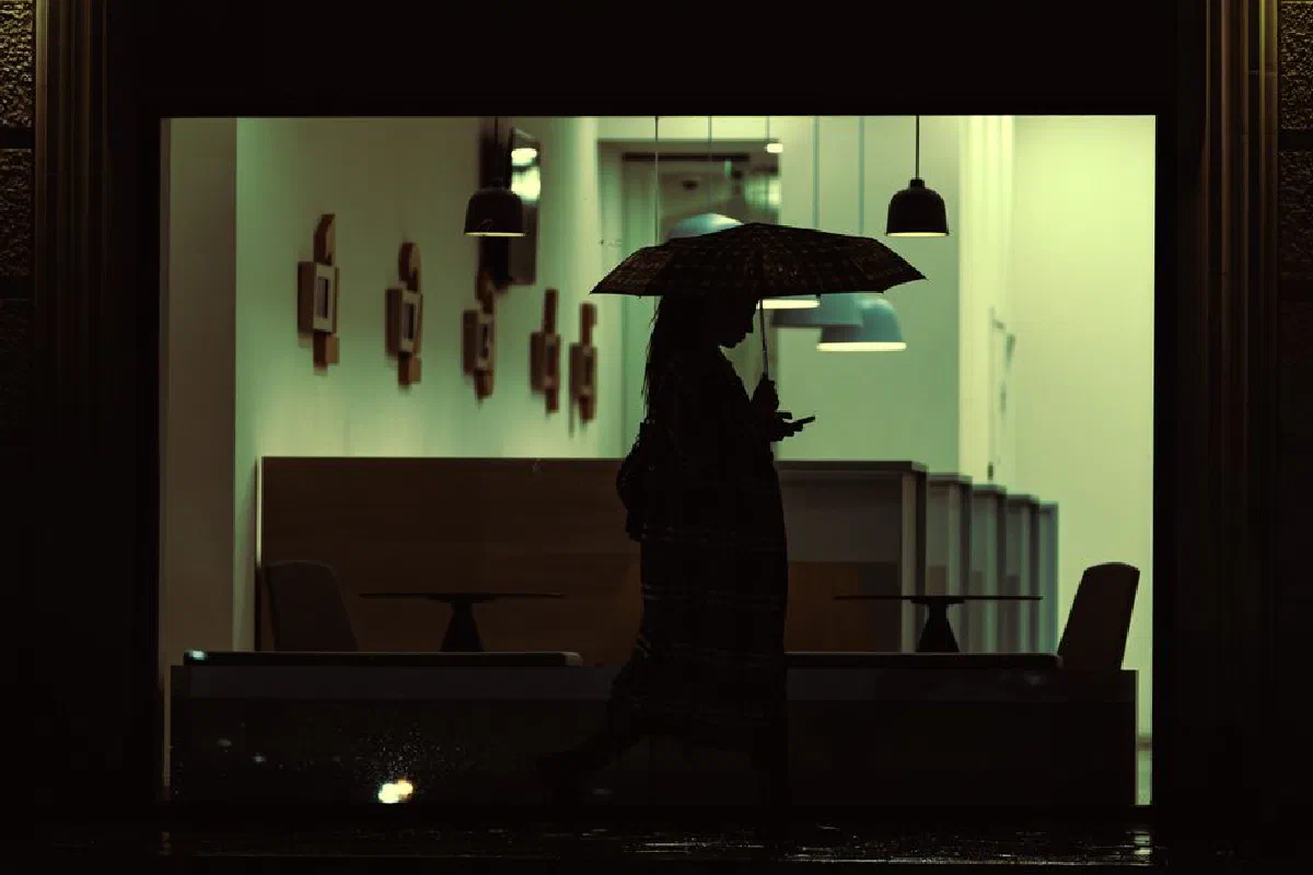 Silhouette of a person with an umbrella walking past a lit interior at night in Kutaisi, Georgia.