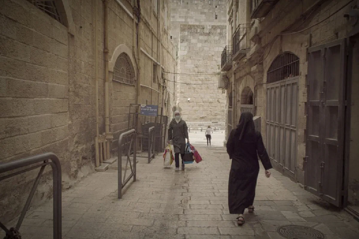 People walking through a narrow alleyway in Jerusalem Old City, showcasing historic architecture.