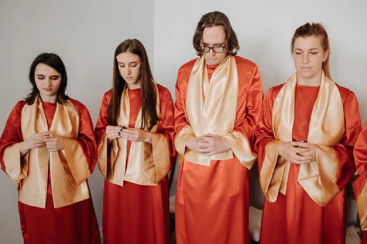 A group of choir members in red robes with gold stoles praying indoors.