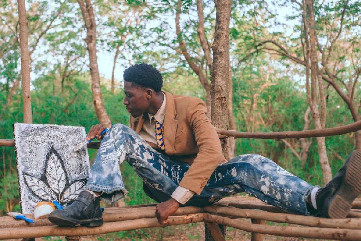 A young male artist actively painting outdoors in Accra, surrounded by nature.
