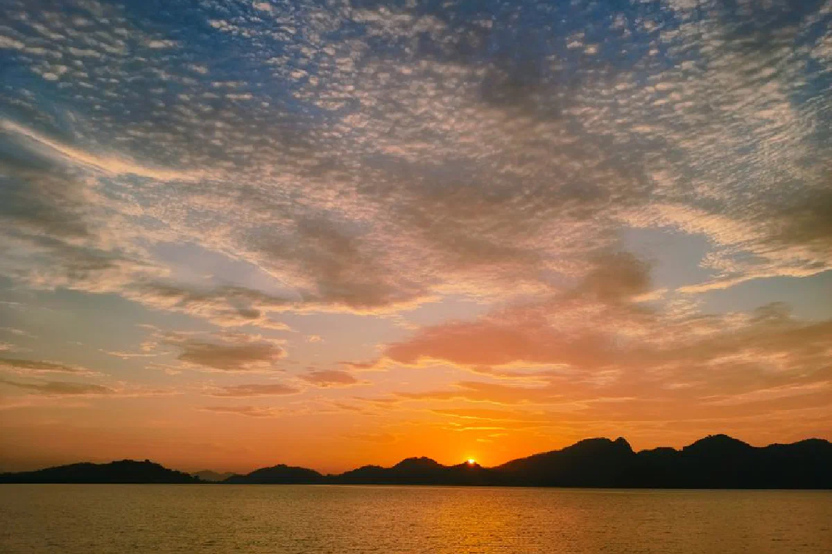 Breathtaking sunset view with vibrant sky over calm ocean and silhouetted mountains.