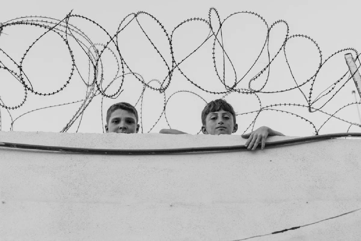 Black and white photo of two boys behind a barbed wire fence in Syria.