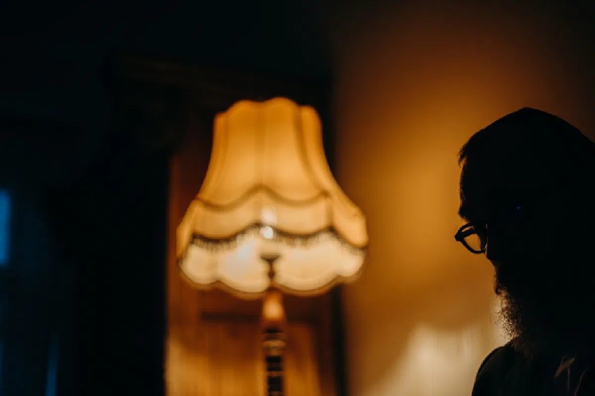 Silhouette of a bearded man beside a vintage lamp casting a warm glow.