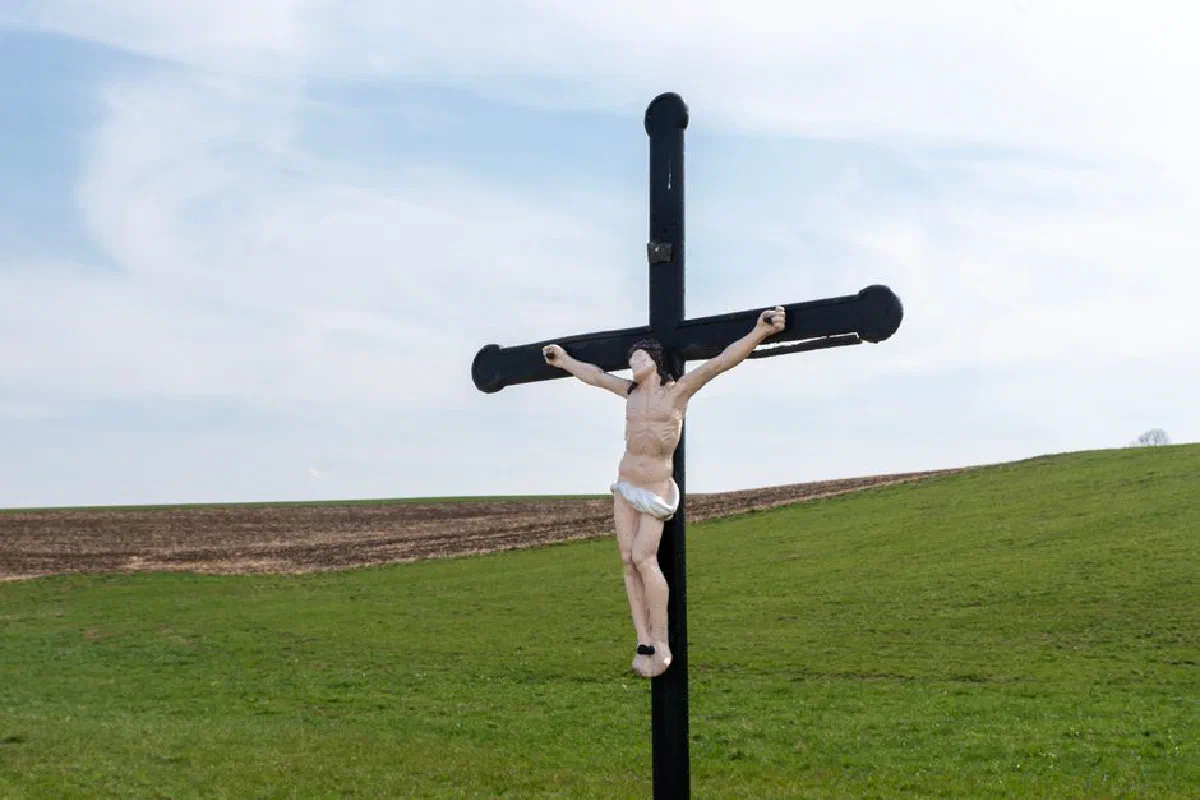 Outdoor crucifixion scene with a cross on a grassy hillside under a clear blue sky.