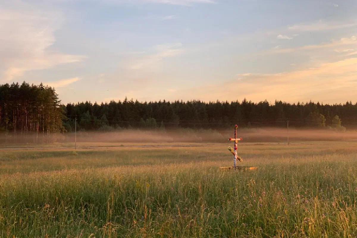 A serene countryside field with a cross in the morning mist and rising sun.