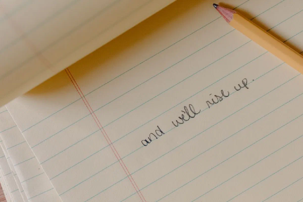 Close-up of a motivational phrase written on a notepad with a pencil.