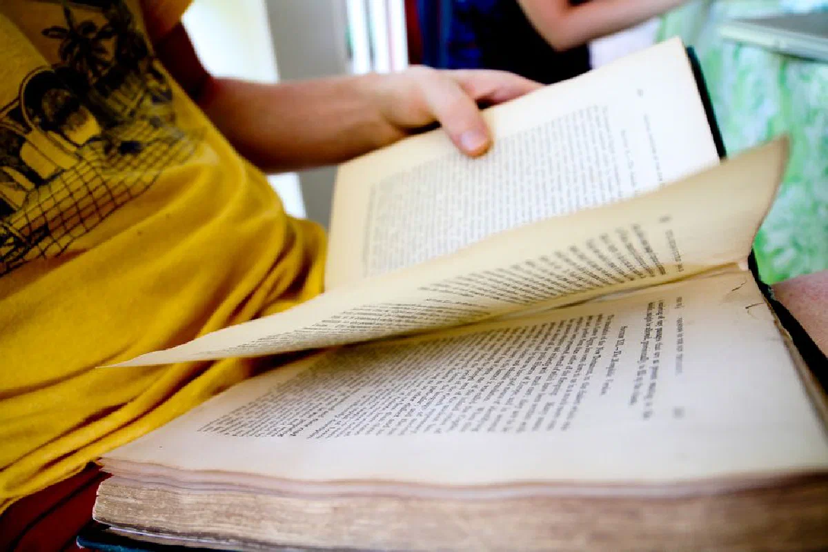 Close-up of a person holding and flipping through an open book indoors.