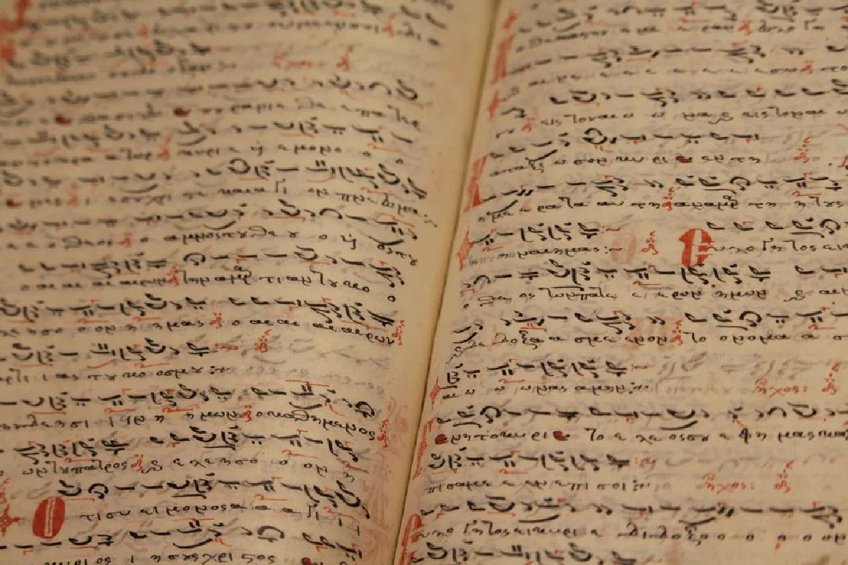 From above of ancient opened book with handwritten inscriptions in black ink in Arabic language on thin pages